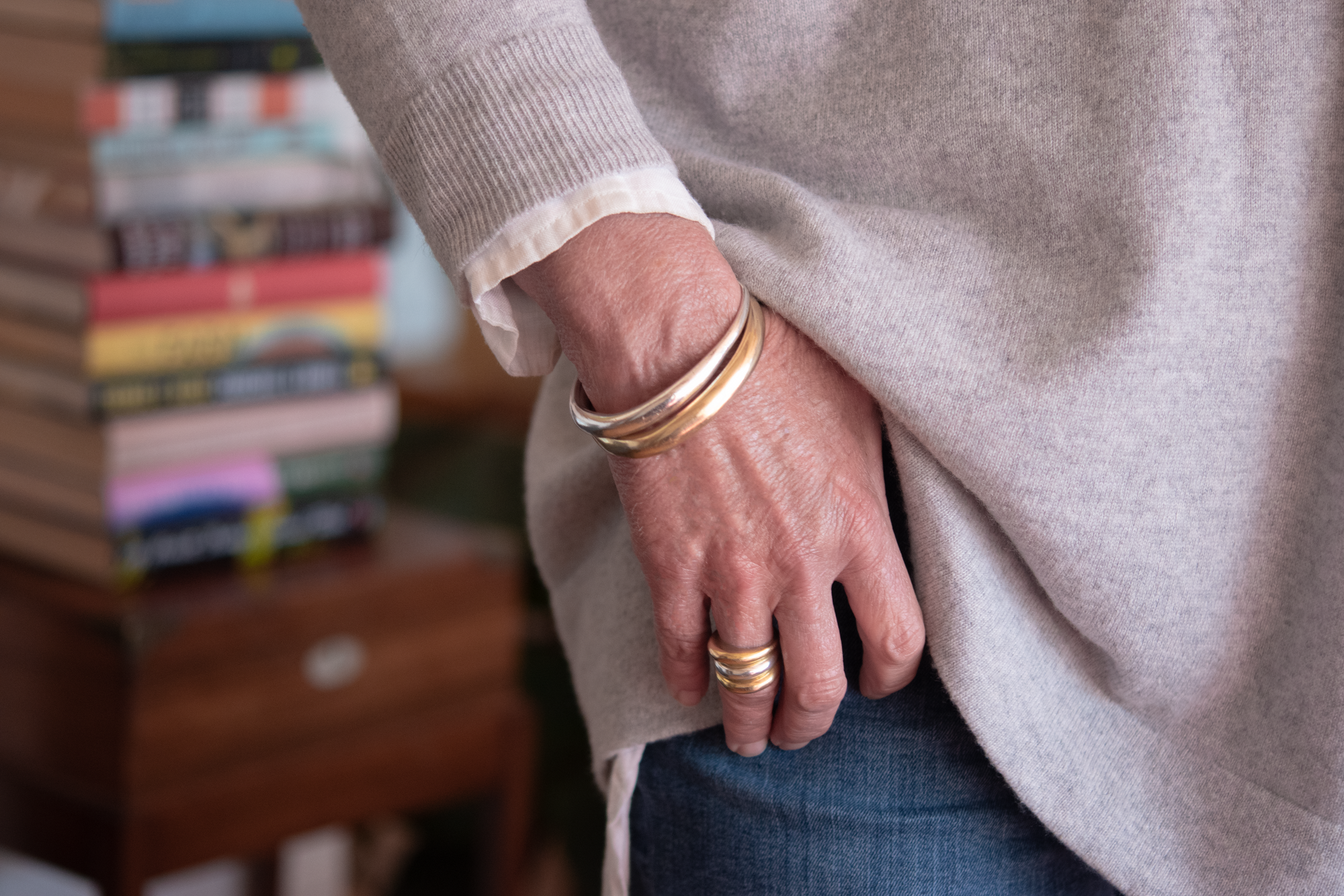 A photo of Liz wearing a mixed metals look with the hand carved minimalist bangle in both brass and sterling silver, as well as the signature ring stack with 18k gold rings.