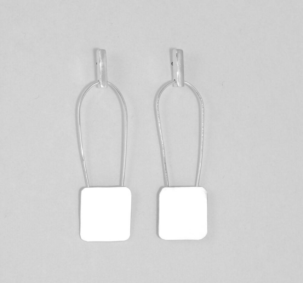 Flat lain photo of the sterling silver bar with Suspended Square Small earrings. 
