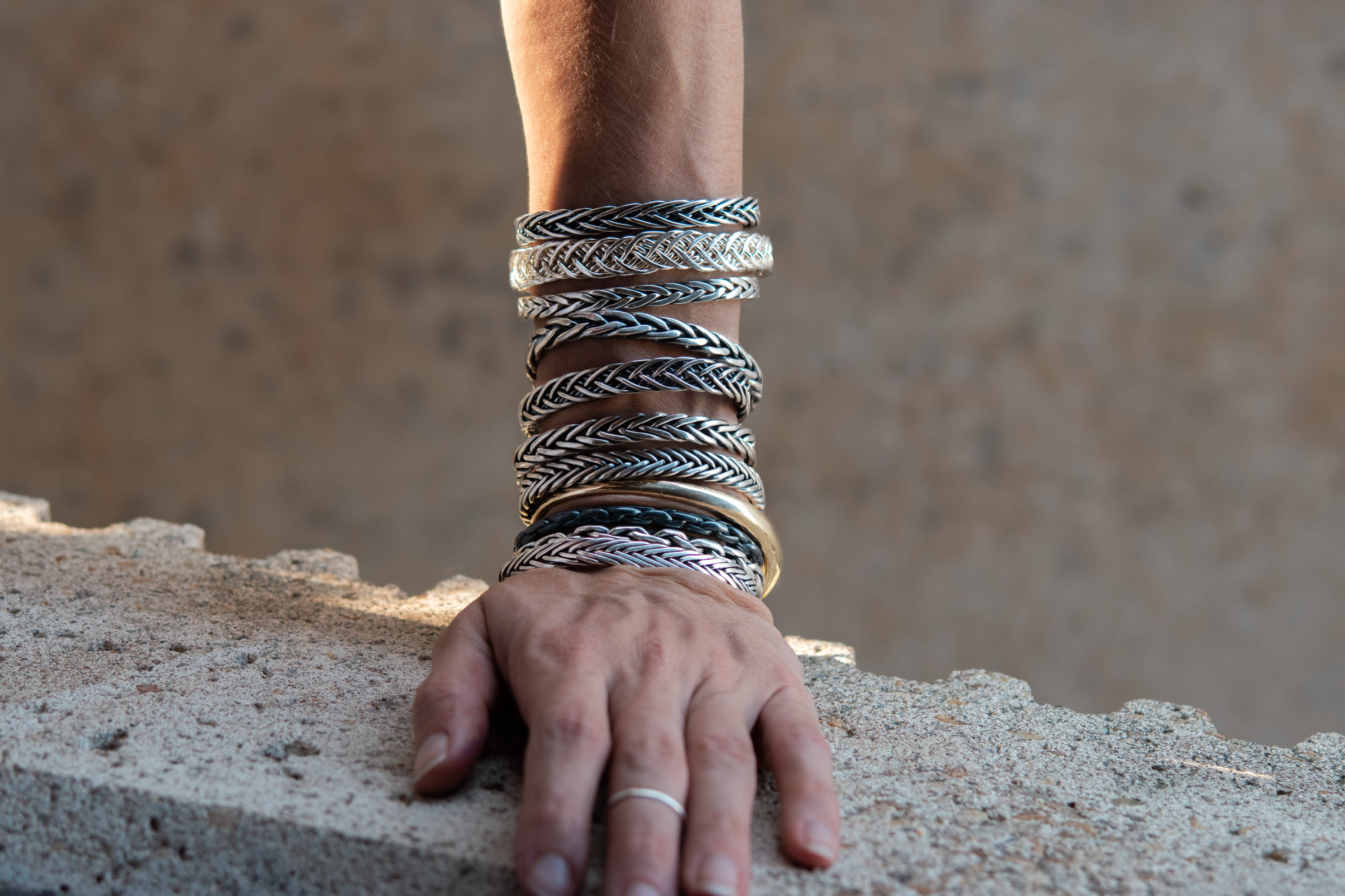 An image of a model wearing a large stack of all the one of a kind, hand woven cuffs available in the ireland collection.