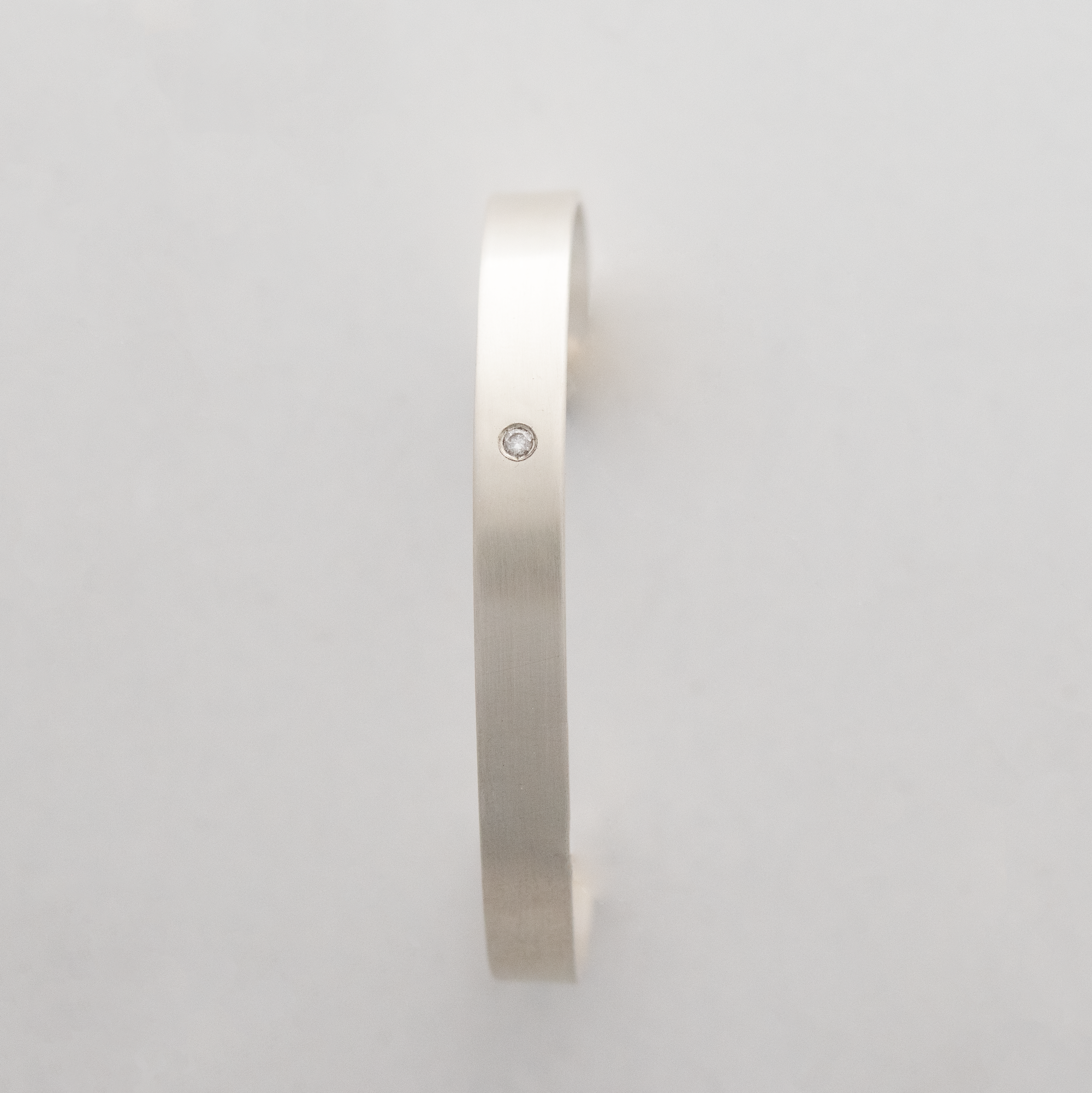 A brushed sterling silver cuff with a 2.5 mm flush set lab grown diamond.