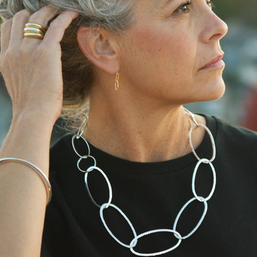 An image of a model wearing the single forged oval collar necklace that features large oval handmade and hand hammered sterling silver links. An airy and bold minimalist jewelry style that sings.