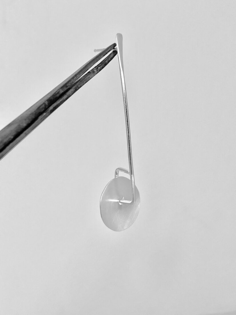 Close up shot of the twirling disc earring suspended from a pair of metalsmithing pliers to show how the twirling disc is freely moving.