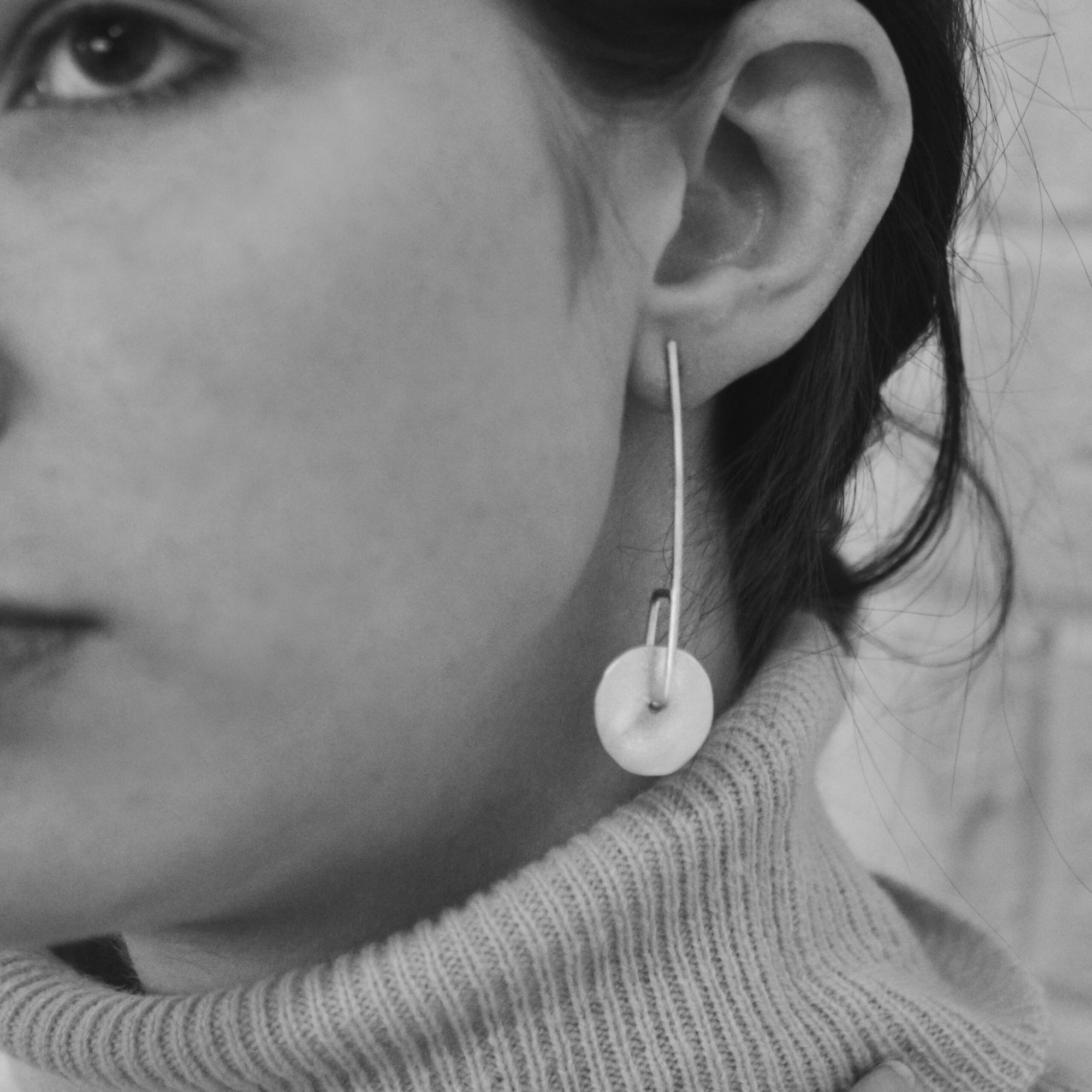 Image shows long twirling disc earrings on a model for scale.