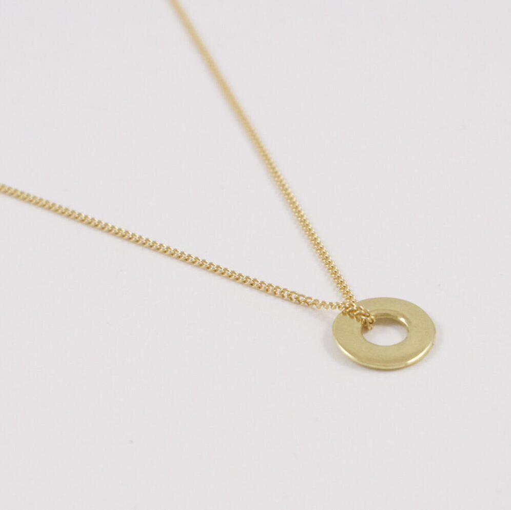 The Mini Ina 18 karat gold necklace lain flat. This close up shows the tiny sculptural disc and the delicate way the chain wraps around it.