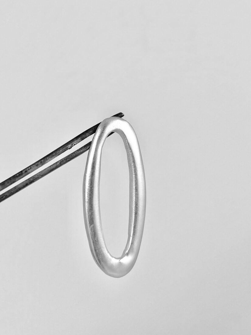 One of the small cast ovals suspended from metalsmithing pliers to show the wabi sabi detail of each oval.