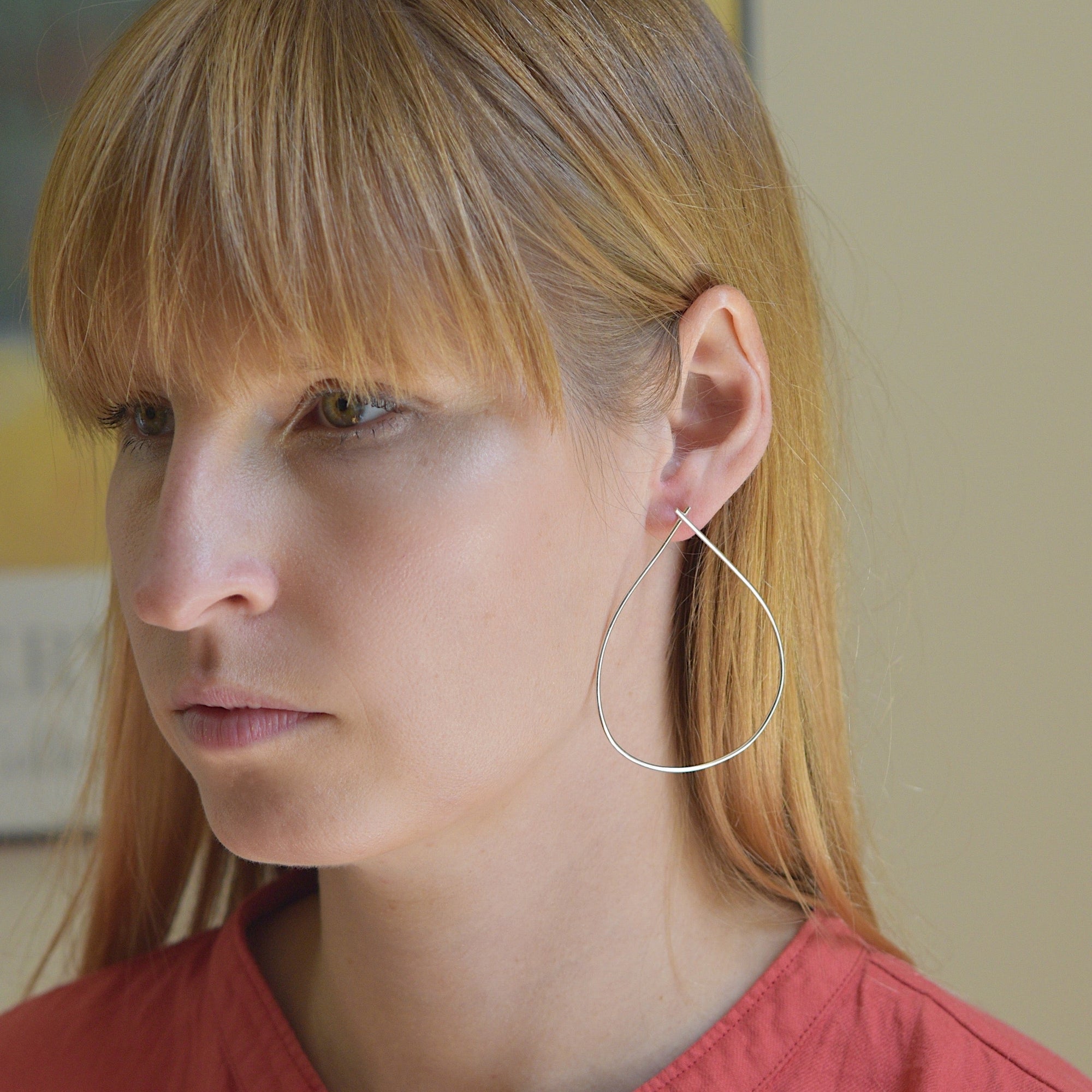 An image of the large teardrop sterling silver wire earrings on a model for scale. These are an interesting and updated take on a hoop style.
